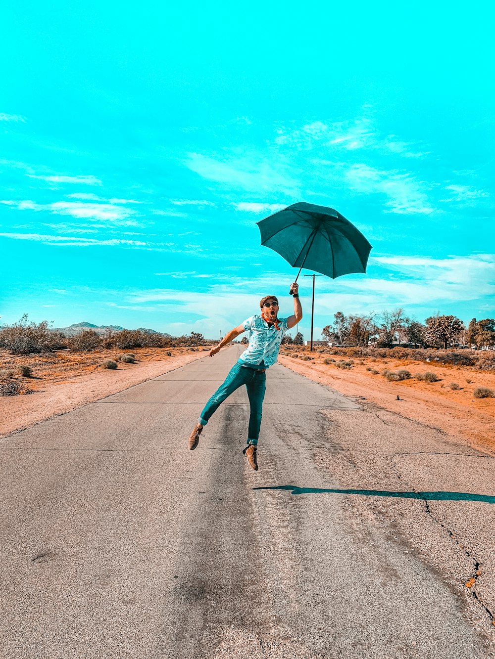 Frau in türkisfarbenem Langarmhemd und blauer Jeans mit Regenschirm beim Gehen auf der Straße während