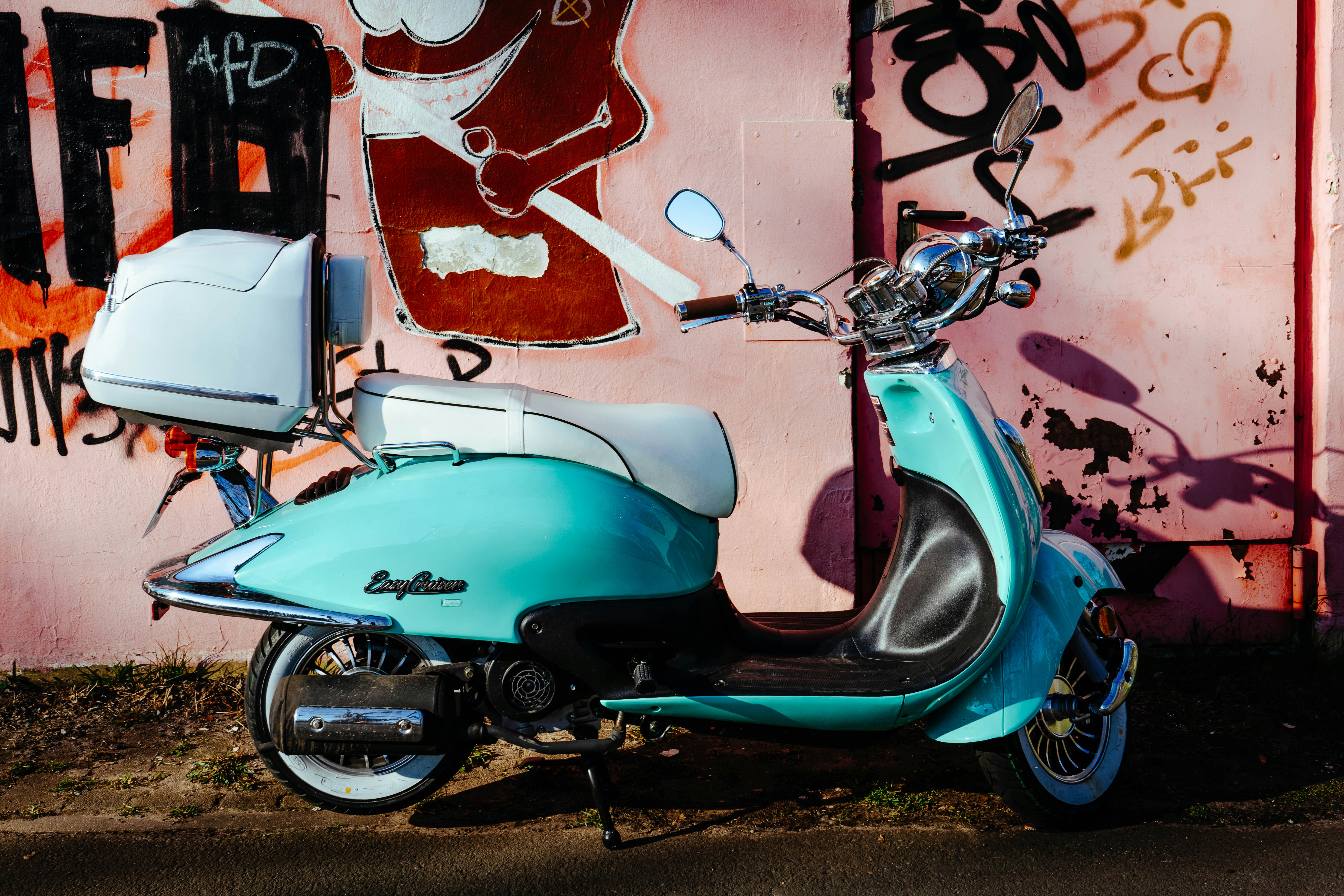 blue and black motor scooter parked beside wall with graffiti