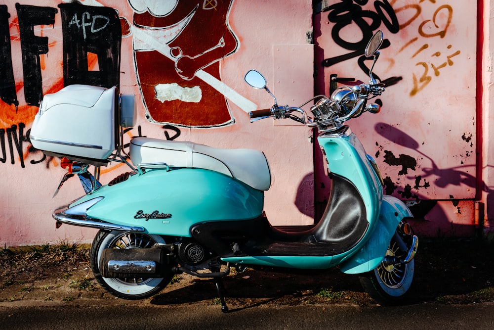blue and black motor scooter parked beside wall with graffiti