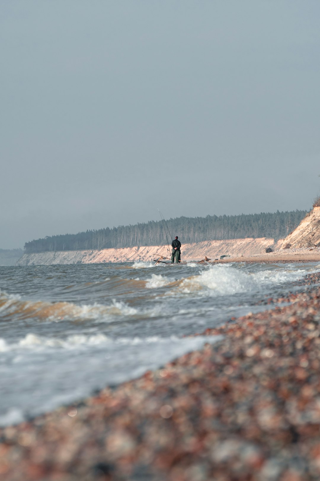 person in black jacket standing on brown rock formation near body of water during daytime