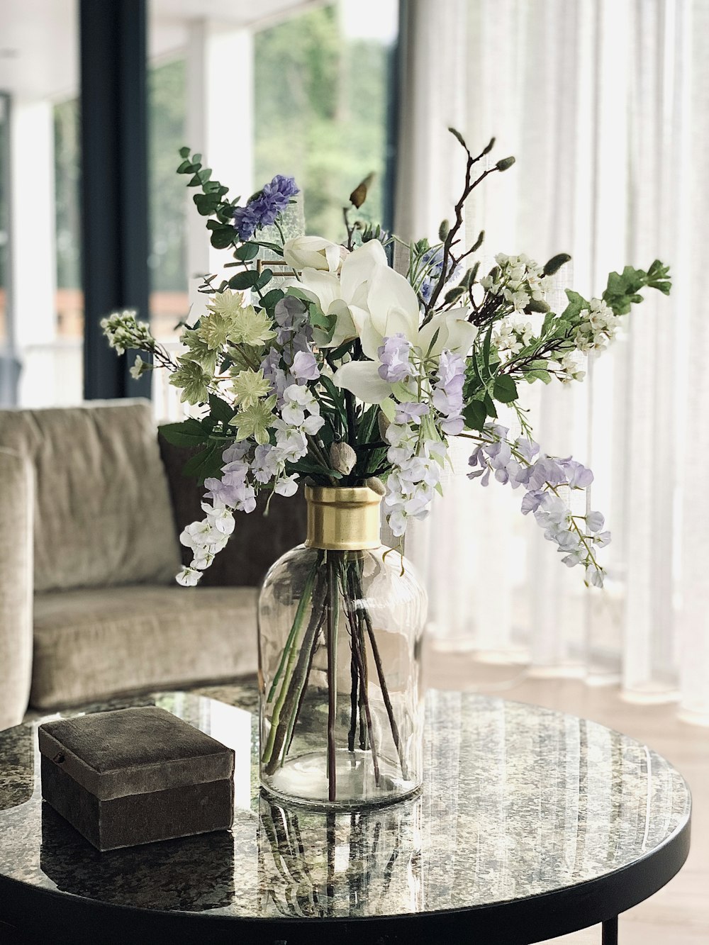 purple flowers in clear glass vase on gray couch