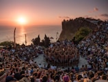people standing on brown rock formation near body of water during sunset