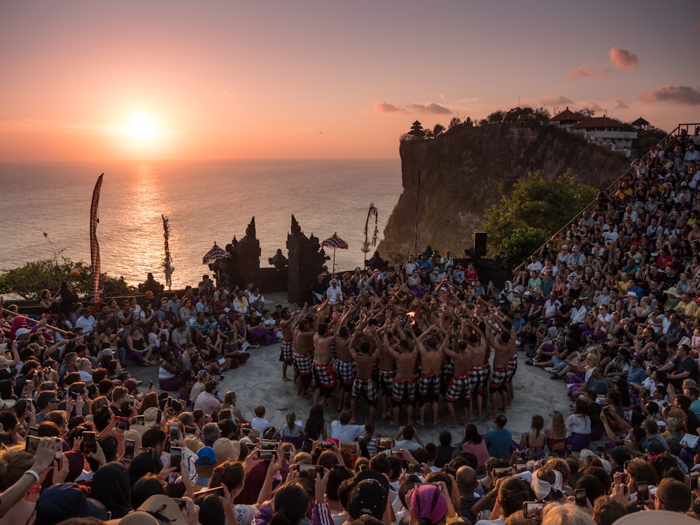 people standing on brown rock formation near body of water during sunset