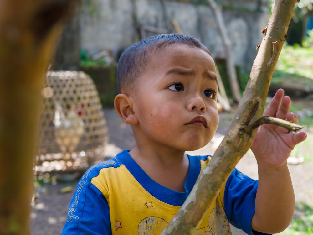 boy in blue and yellow crew neck shirt holding brown wooden stick during daytime