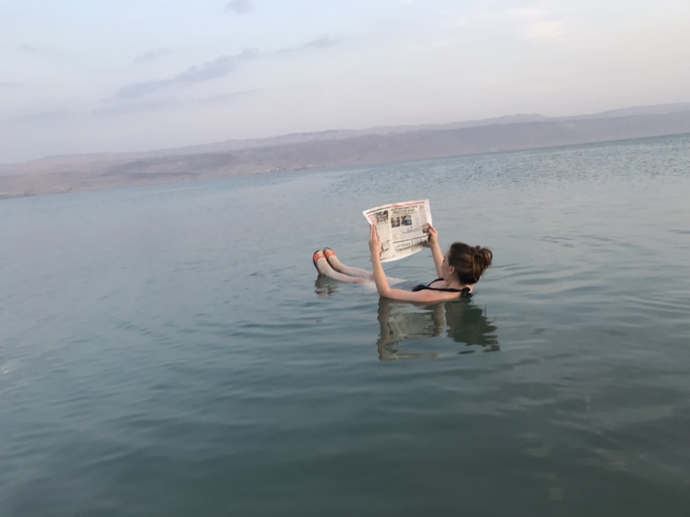 woman in body of water reading book