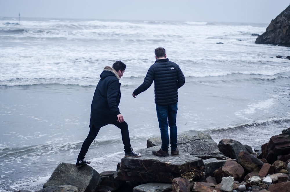 man and woman standing on rock near sea during daytime