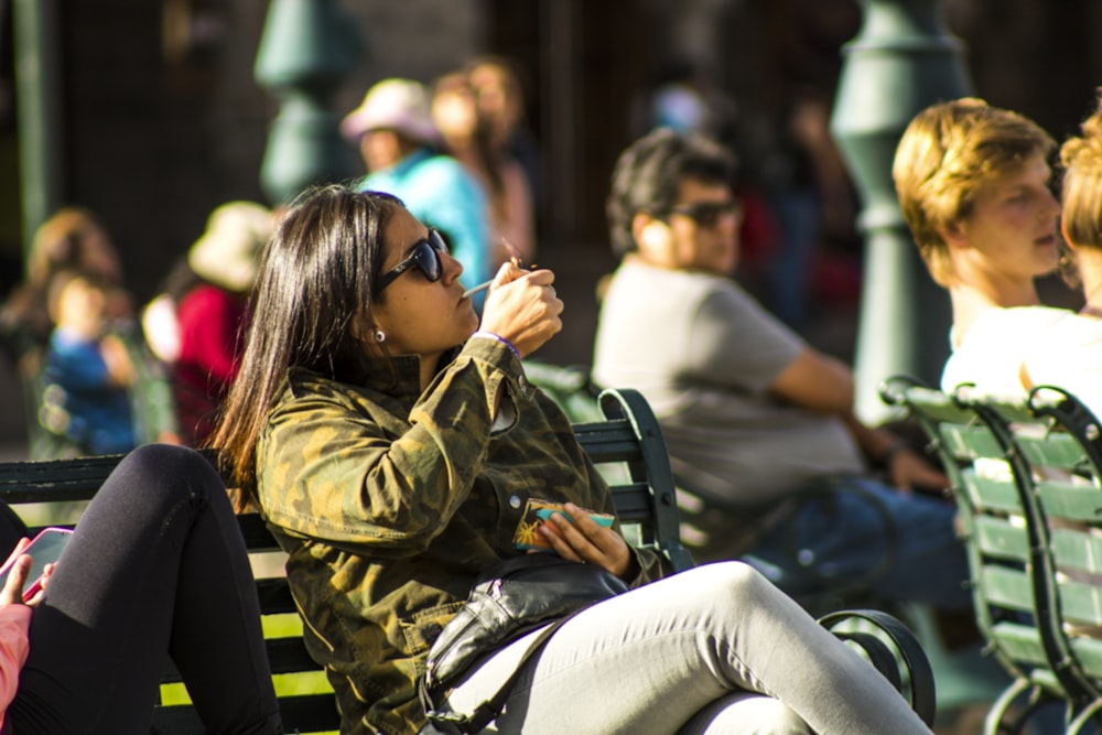 woman in green and brown camouflage jacket and gray pants sitting on bench during daytime