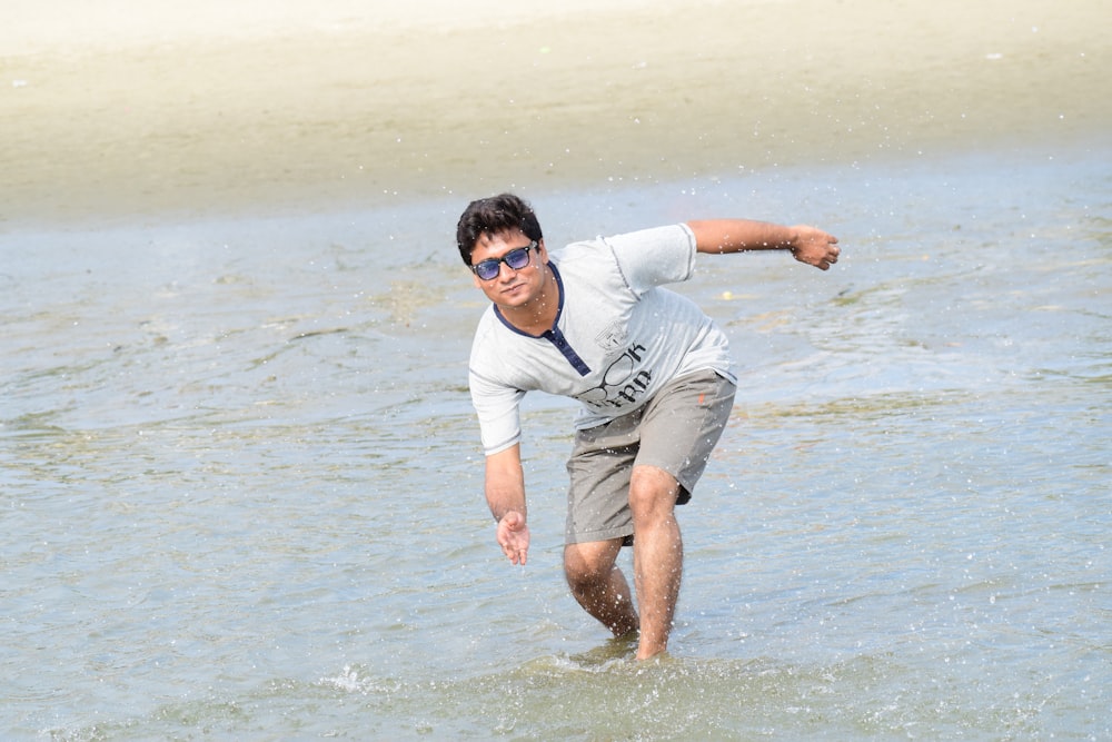 man in white t-shirt and brown shorts standing on water during daytime