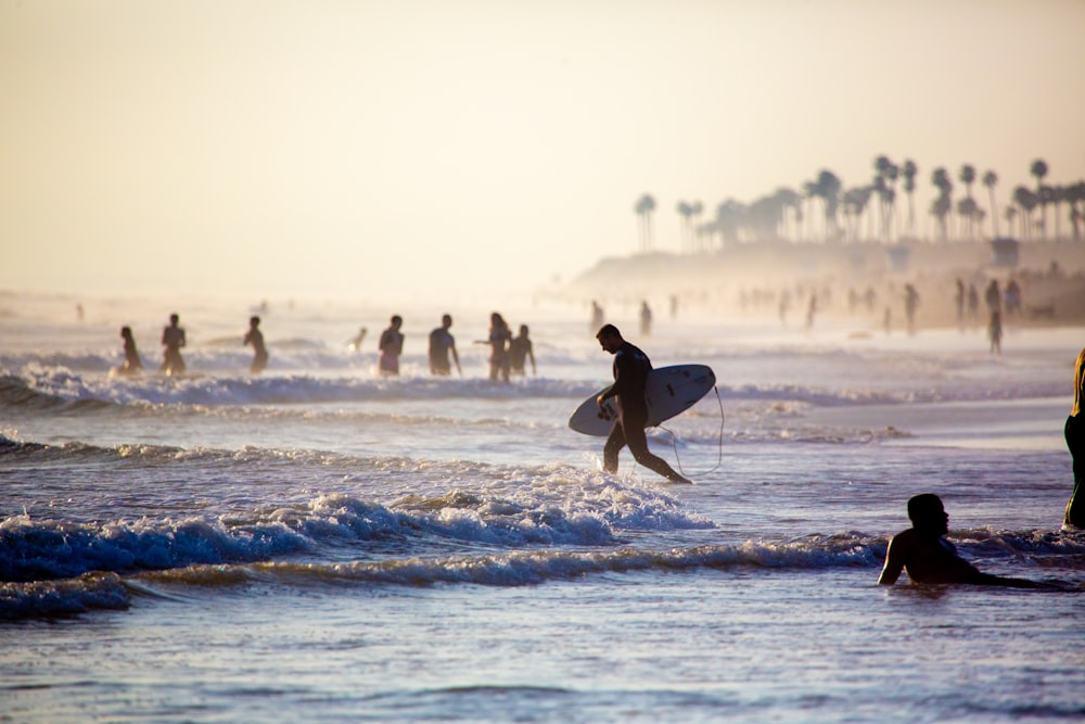 man in black wet suit carrying white surfboard on beach during daytime