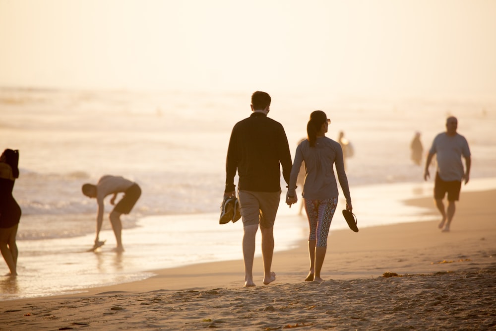 homem e mulher de mãos dadas enquanto caminham na praia durante o dia
