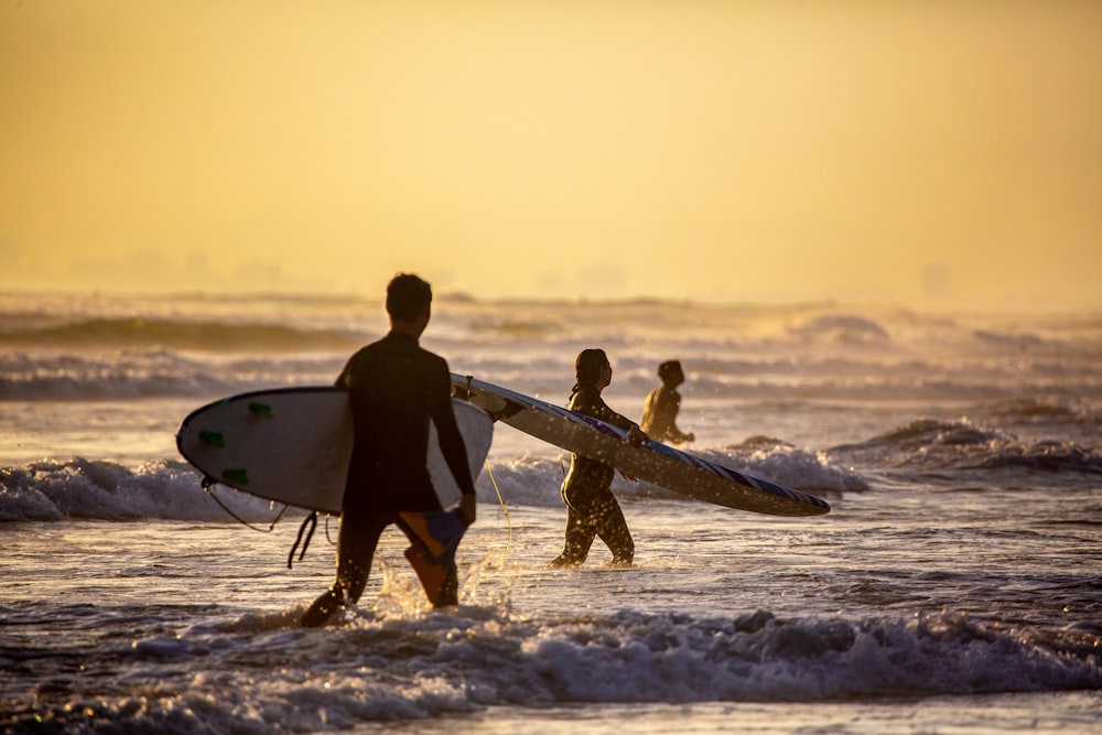 silhouette of 2 men holding surfboard walking on beach during sunset