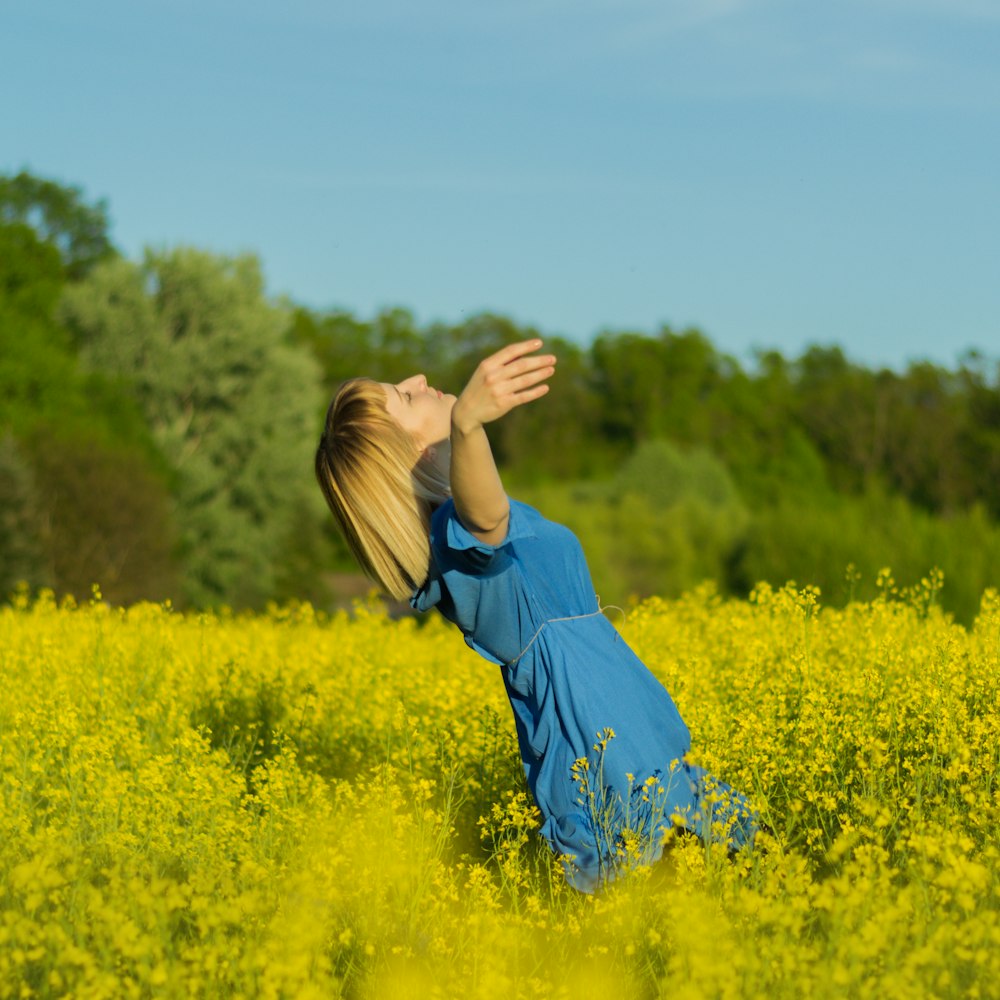 woman in blue long sleeve shirt standing on yellow flower field during daytime