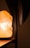 The image features a warmly lit Himalayan salt lamp on a wooden surface, casting a soft glow. The background is out of focus, with a dark vertical element partially visible to the right.