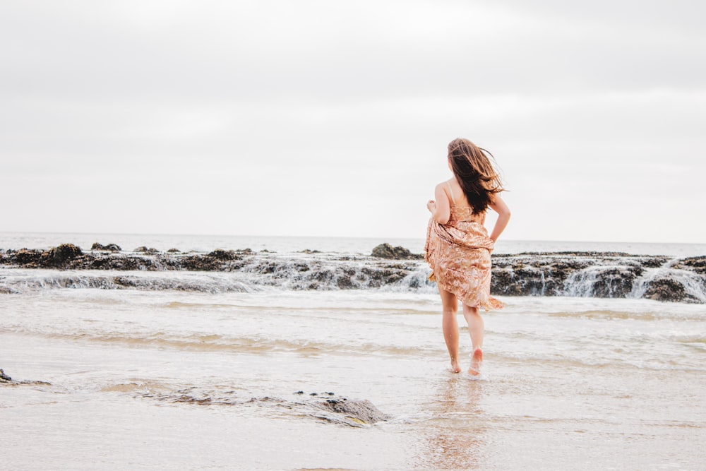 woman in white dress walking on beach during daytime