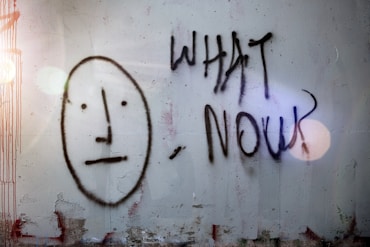 Graffiti showing a nonplussed face and "what now?"