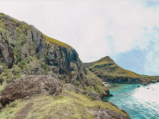 green and brown mountain beside body of water during daytime in Batanes Philippines