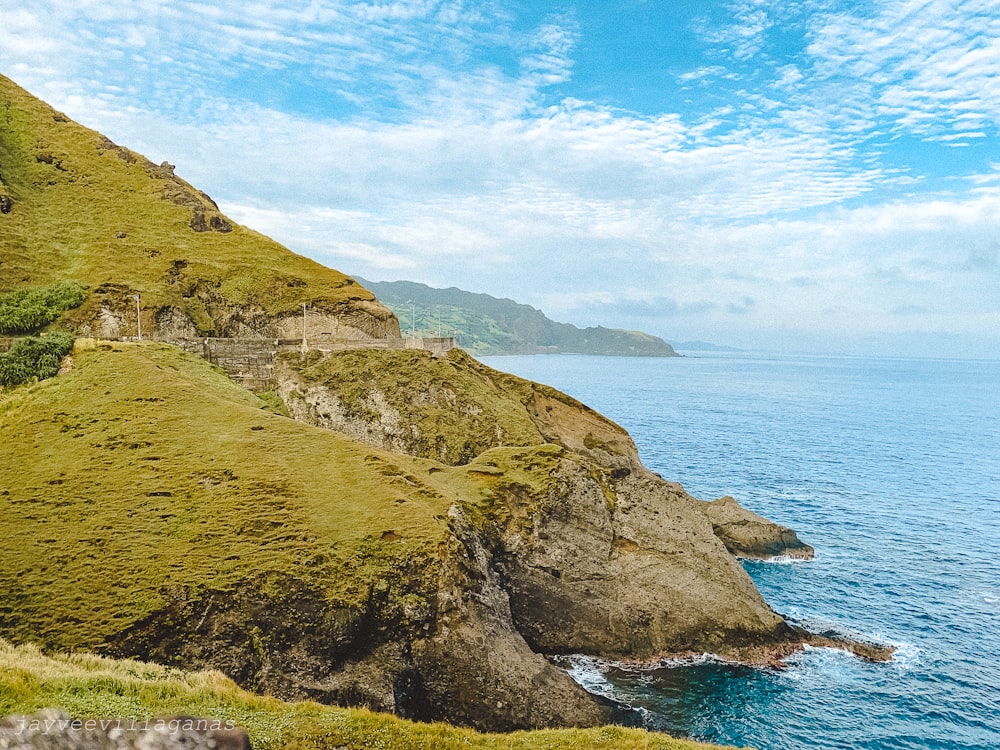 montaña verde y marrón al lado del mar bajo el cielo azul durante el día