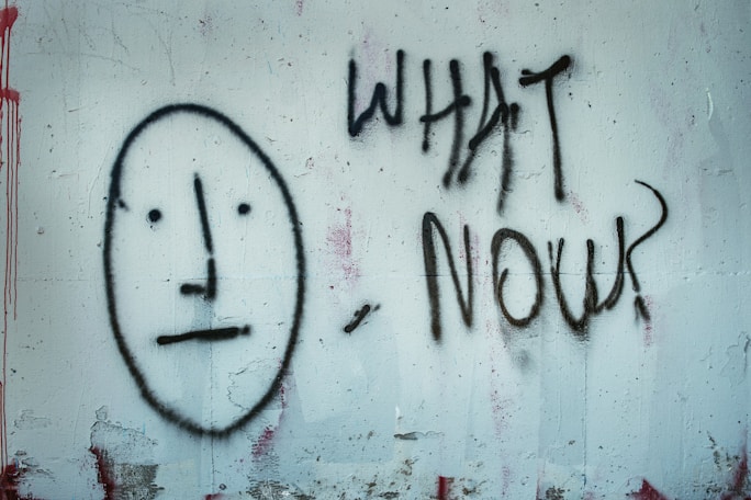 A face on a wall with the writing, "What now?"