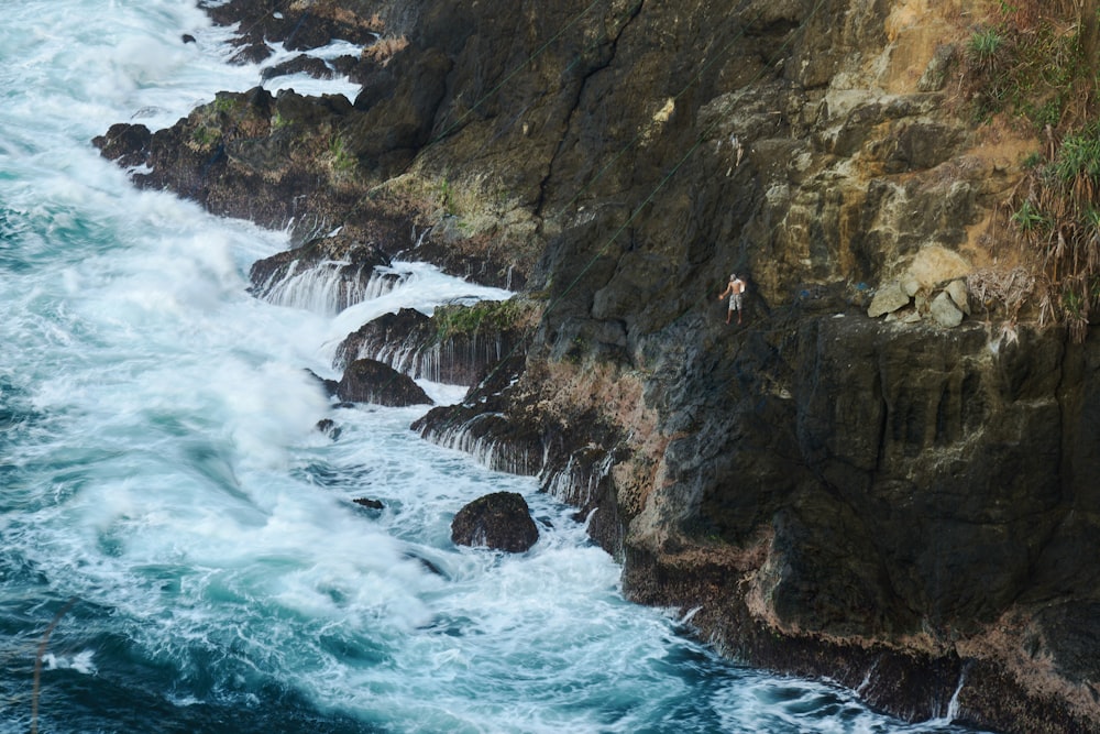 water waves hitting brown rocky mountain during daytime