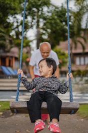 boy in black and white checkered dress shirt sitting on blue swing during daytime