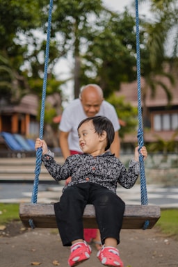 boy in black and white checkered dress shirt sitting on blue swing during daytime