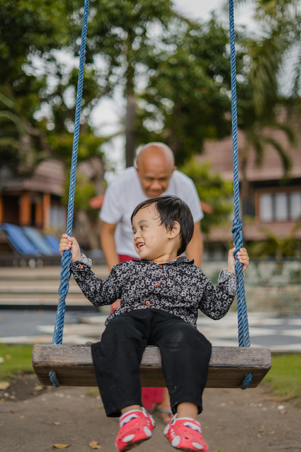 boy in black and white checkered dress shirt sitting on blue swing during daytime