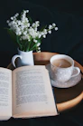 An open book, a cup of coffee, and lily of the valley on a tray