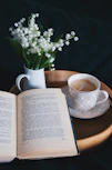 An open book, a cup of coffee, and lily of the valley on a tray
