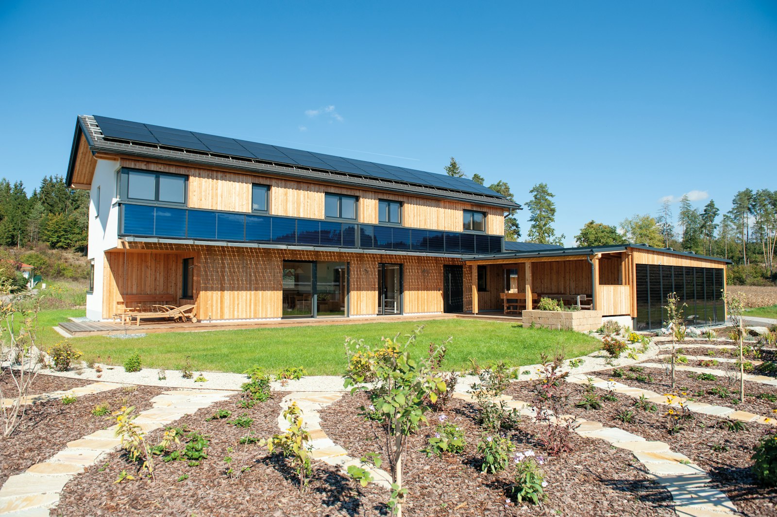 Sustainable timber clad home with rooftop solar panels set in a landscaped garden, demonstrating low carbon residential design