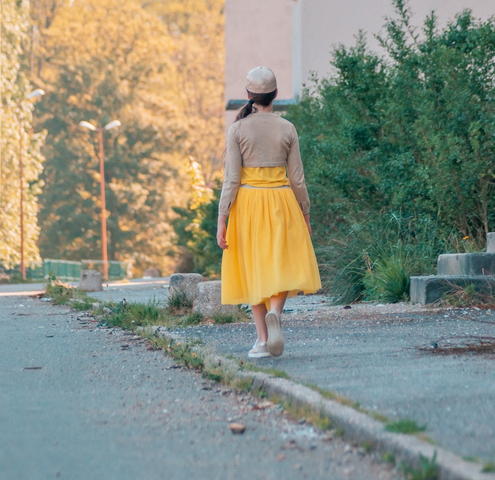 girl in yellow dress walking on gray concrete road during daytime