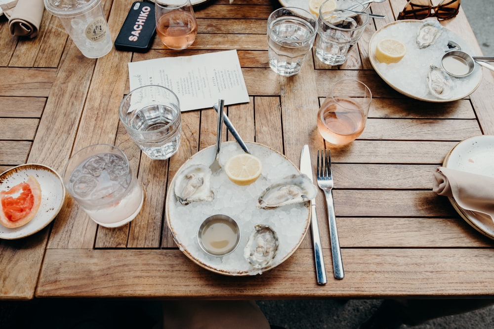 colheres de aço inoxidável na placa de cerâmica branca ao lado do vidro de beber na mesa de madeira marrom