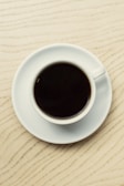Close-up of a coffee cup on a matte black table with architectural blueprints underneath.