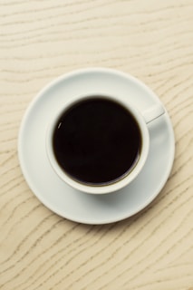A close-up of a steaming cup of black coffee on a wooden table with zero sugar branding visible.