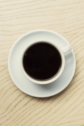 Close-up of a coffee cup on a matte black table with architectural blueprints underneath.