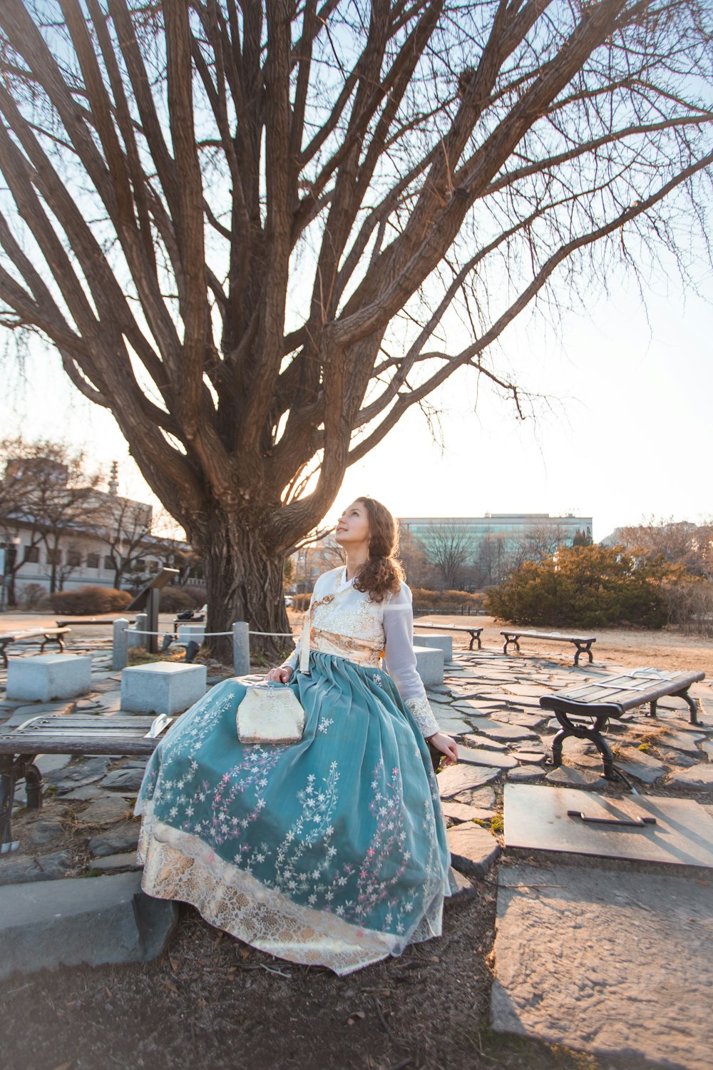 woman in white long sleeve shirt and blue floral skirt sitting on brown wooden bench during