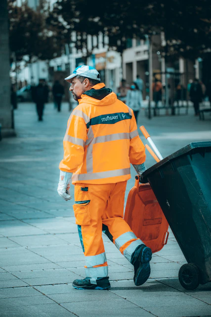 Sanitation worker moving a trash bin along a city sidewalk