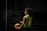 A person wearing a green and yellow sports jersey with the name and number 'Jurado 10' is standing outdoors holding a blue and yellow volleyball. The setting appears to be shadowy, possibly a sports court or outdoor area with railings visible in the background.