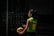 A person wearing a green and yellow sports jersey with the name and number 'Jurado 10' is standing outdoors holding a blue and yellow volleyball. The setting appears to be shadowy, possibly a sports court or outdoor area with railings visible in the background.