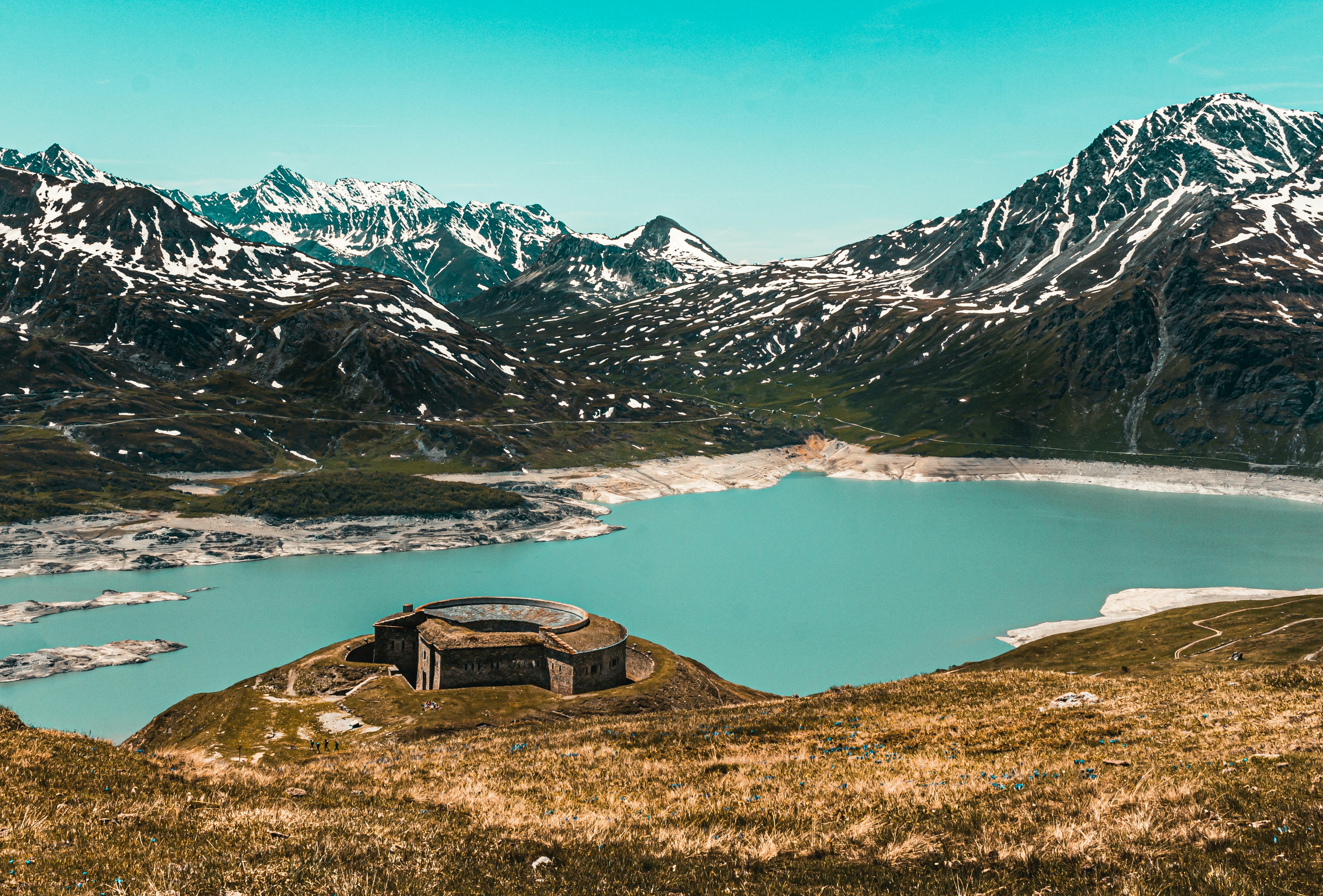 brown wooden house on green grass field near lake and snow covered mountains during daytime