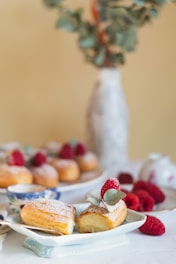 A pastel in soft pink and beige tones decorated with fresh berries and nuts on a rustic wooden table.