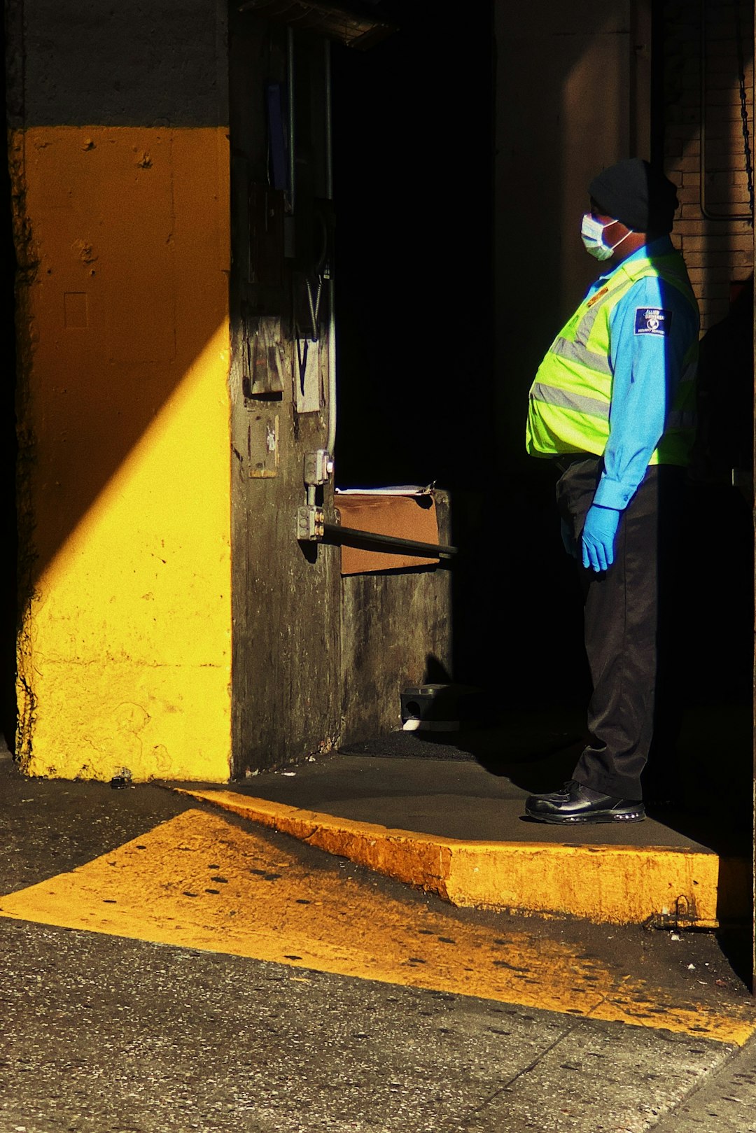 man in green jacket and black pants standing beside yellow painted wall
