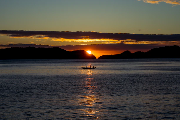 Golden sunset over calm lagoon waters with a traditional fishing boat silhouetted.