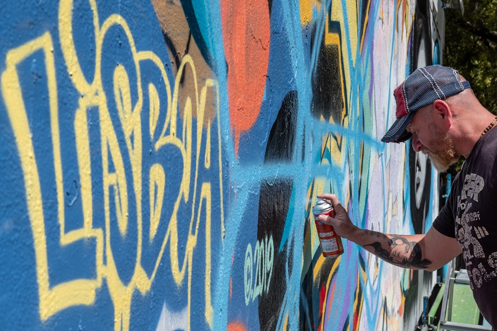 man in black t-shirt and blue denim jeans standing on graffiti wall