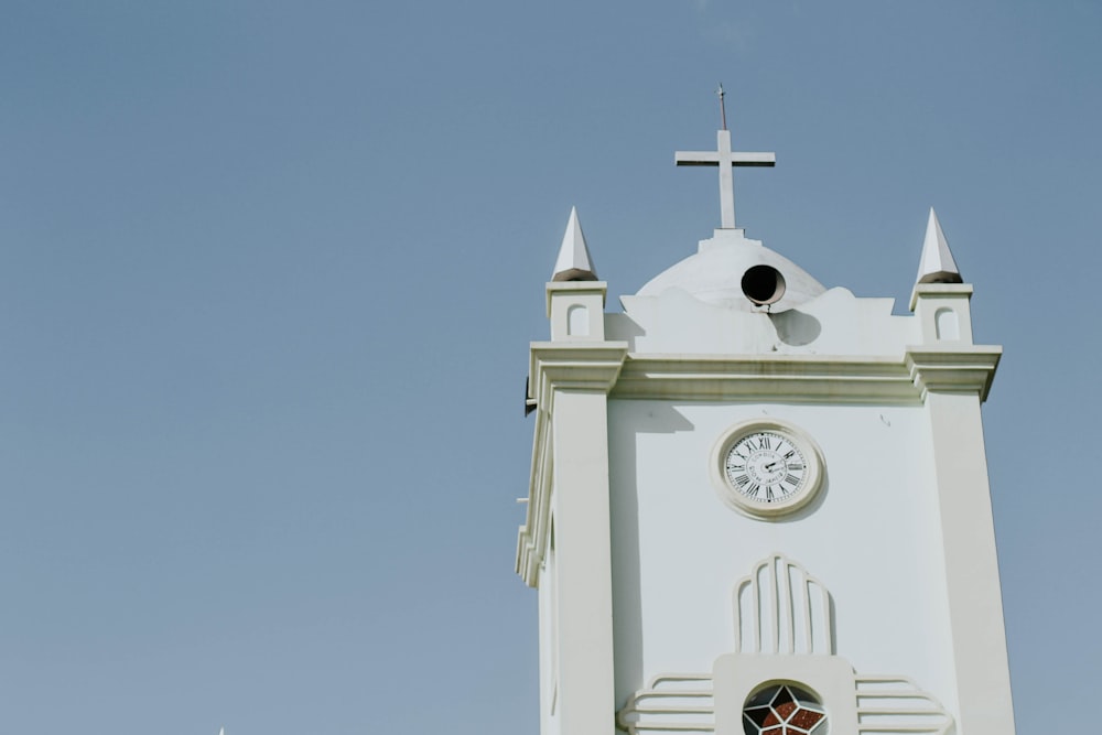 a white clock tower with a cross on top
