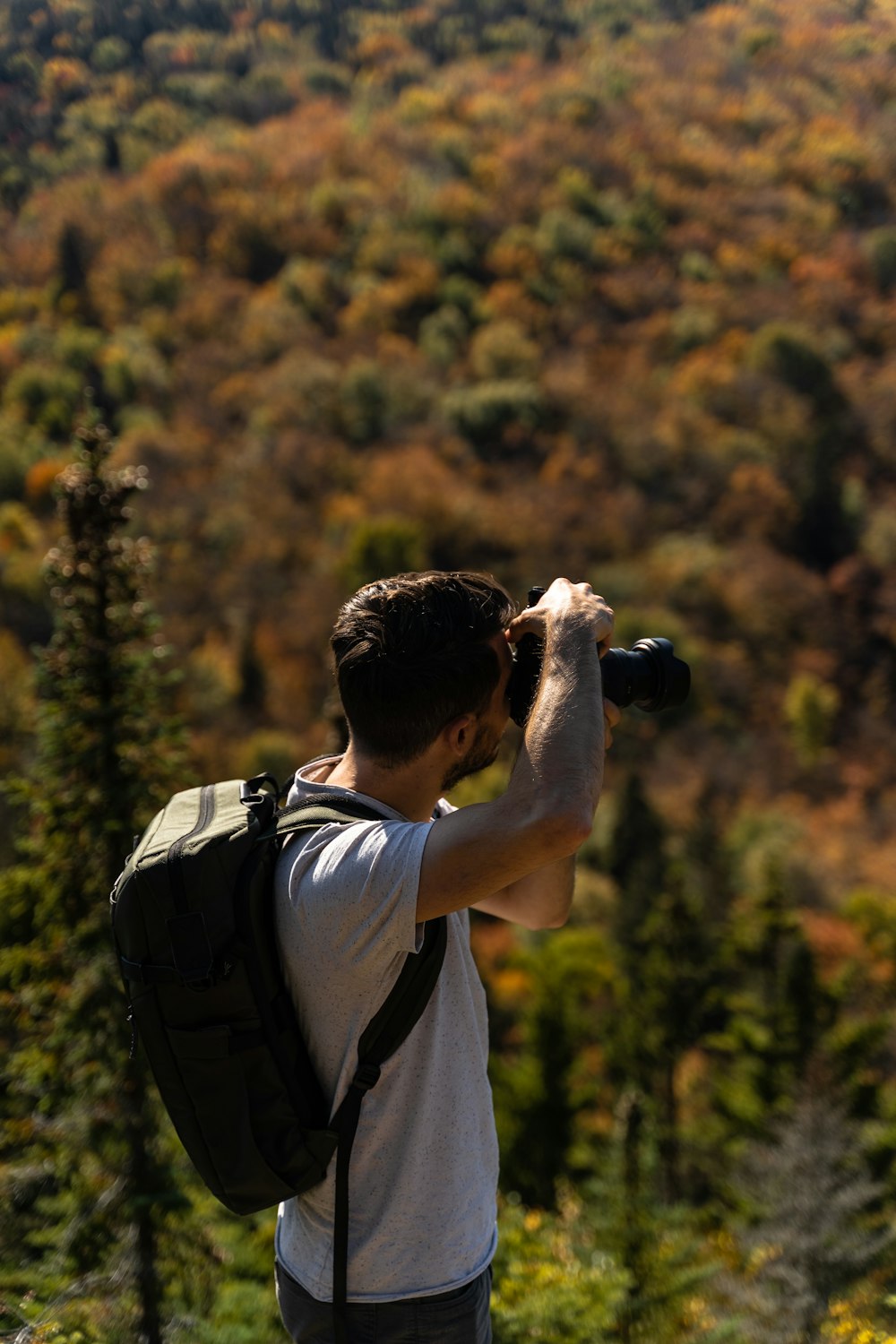 Hombre con camiseta blanca sosteniendo una cámara DSLR negra durante el día