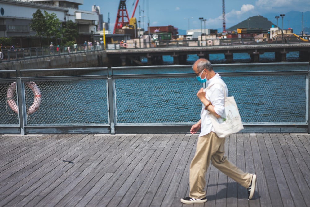 白いシャツと茶色のズボンを着た男が昼間、木製の波止場を歩いている