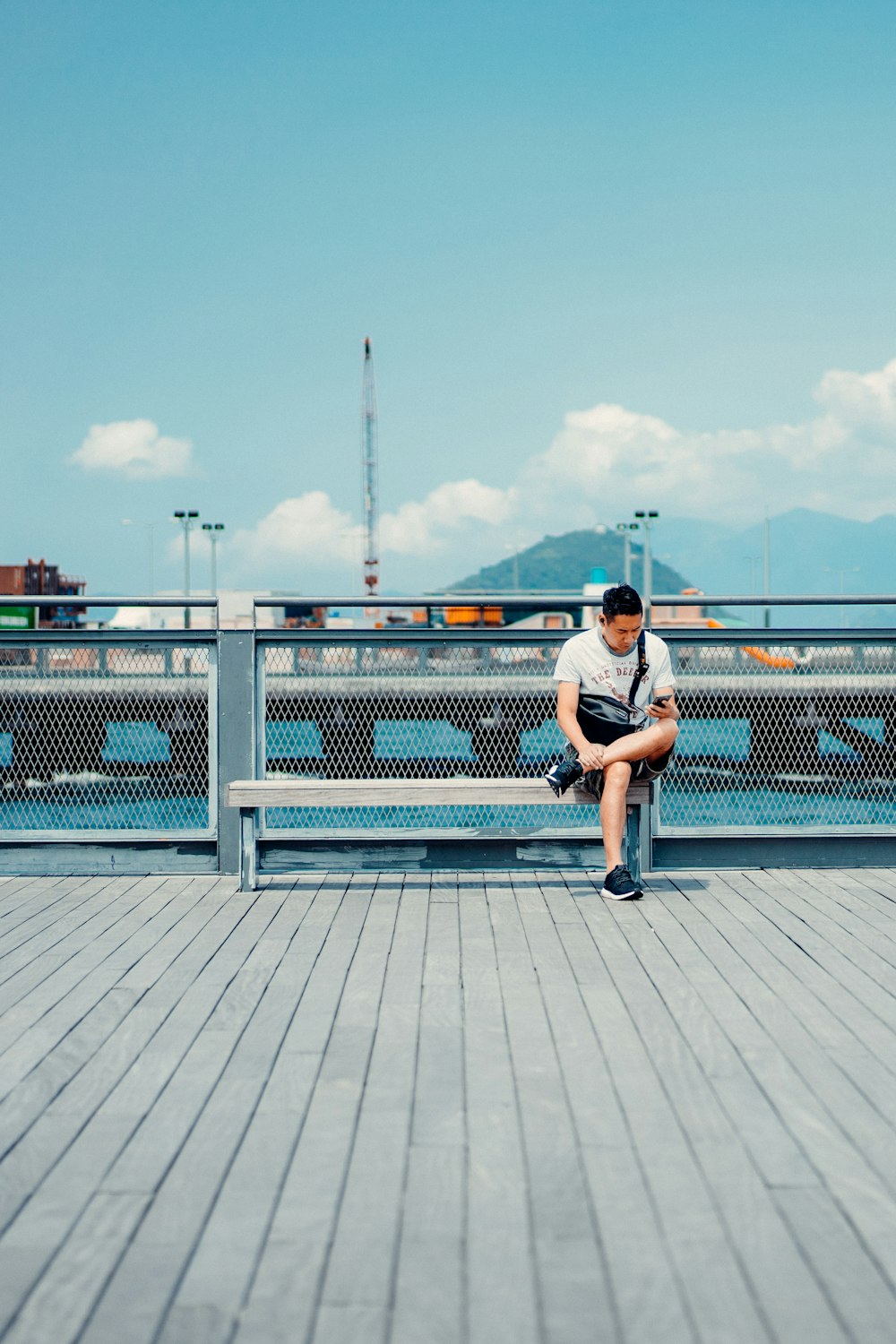 man in white t-shirt and blue shorts sitting on white metal fence during daytime