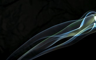 Elegant, wispy smoke trails flowing across a dark background with a translucent, ethereal quality. The smoke appears to be illuminated, revealing subtle hints of color transition.