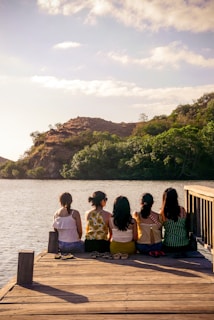 group of people sitting on brown wooden bench near body of water during daytime