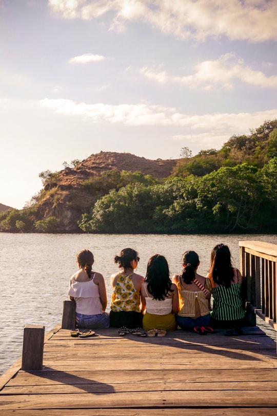 group of people sitting on brown wooden bench near body of water during daytime in Labuan Bajo Indonesia